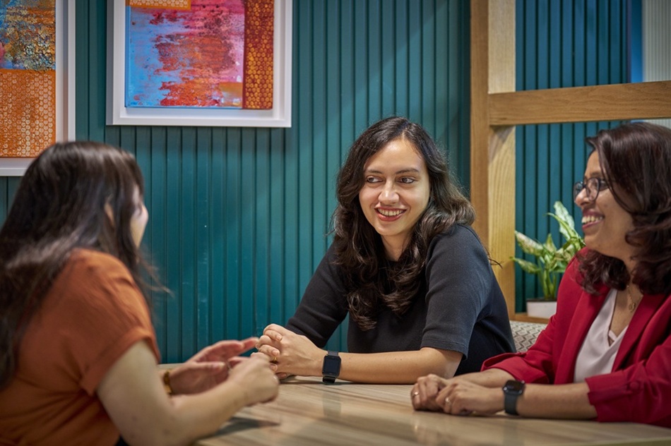 Three people seated around a table in a modern office space, engaged in a group discussion.