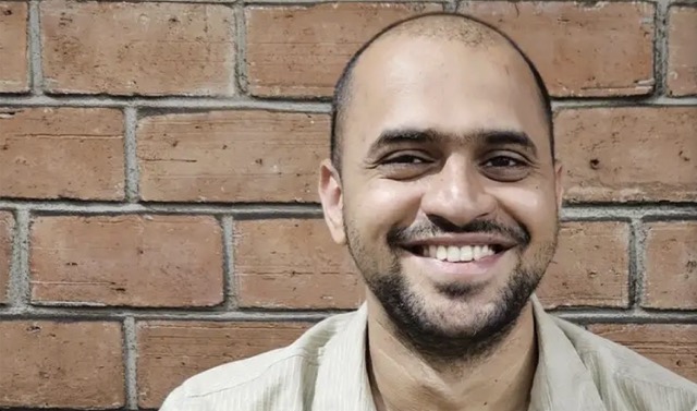 Professional headshot of man with beard on brick background