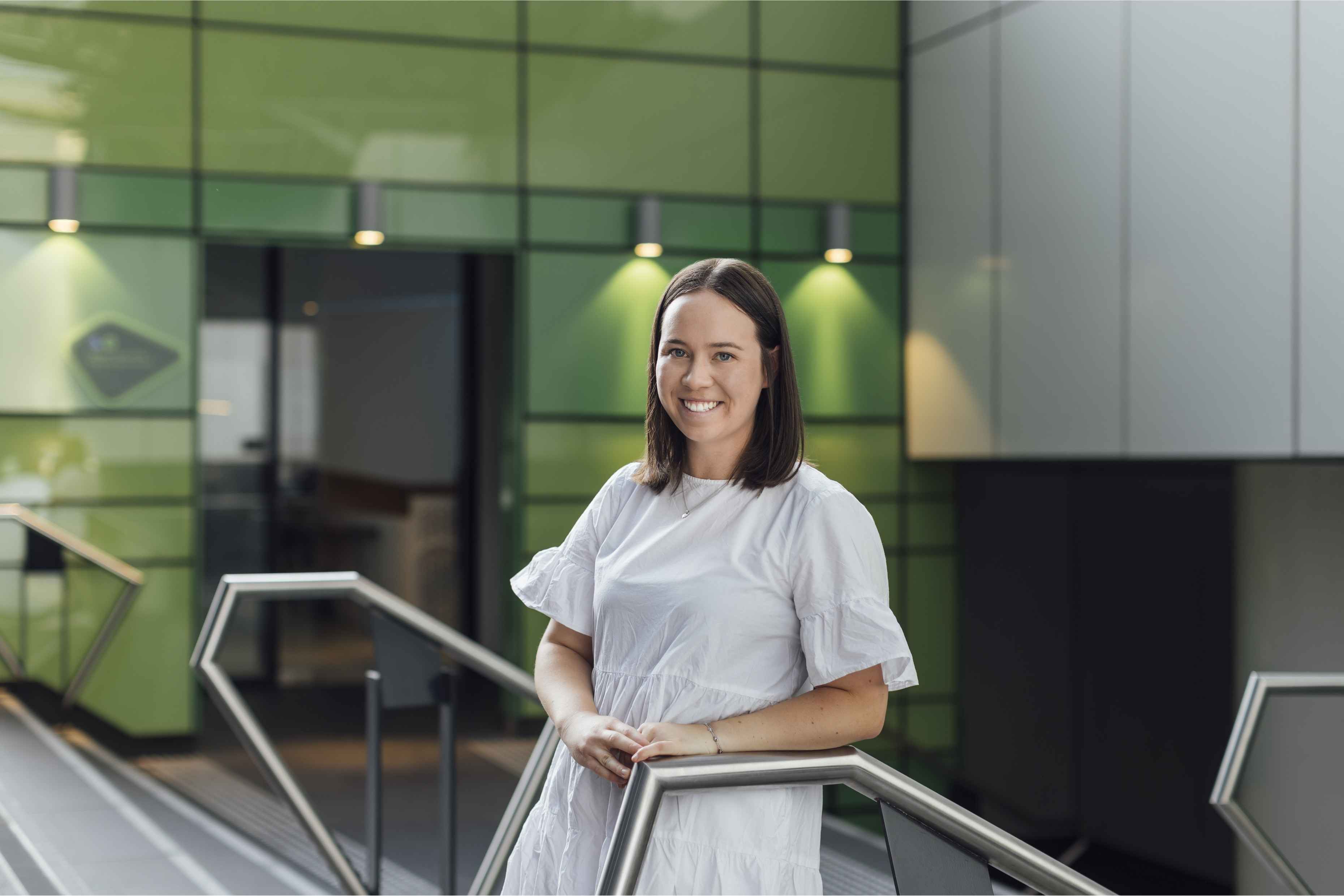 Three colleagues smiling and talking around a laptop in a modern office.