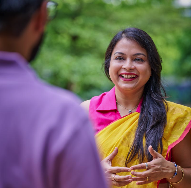 Smiling woman in yellow sari talking with colleague outdoors.