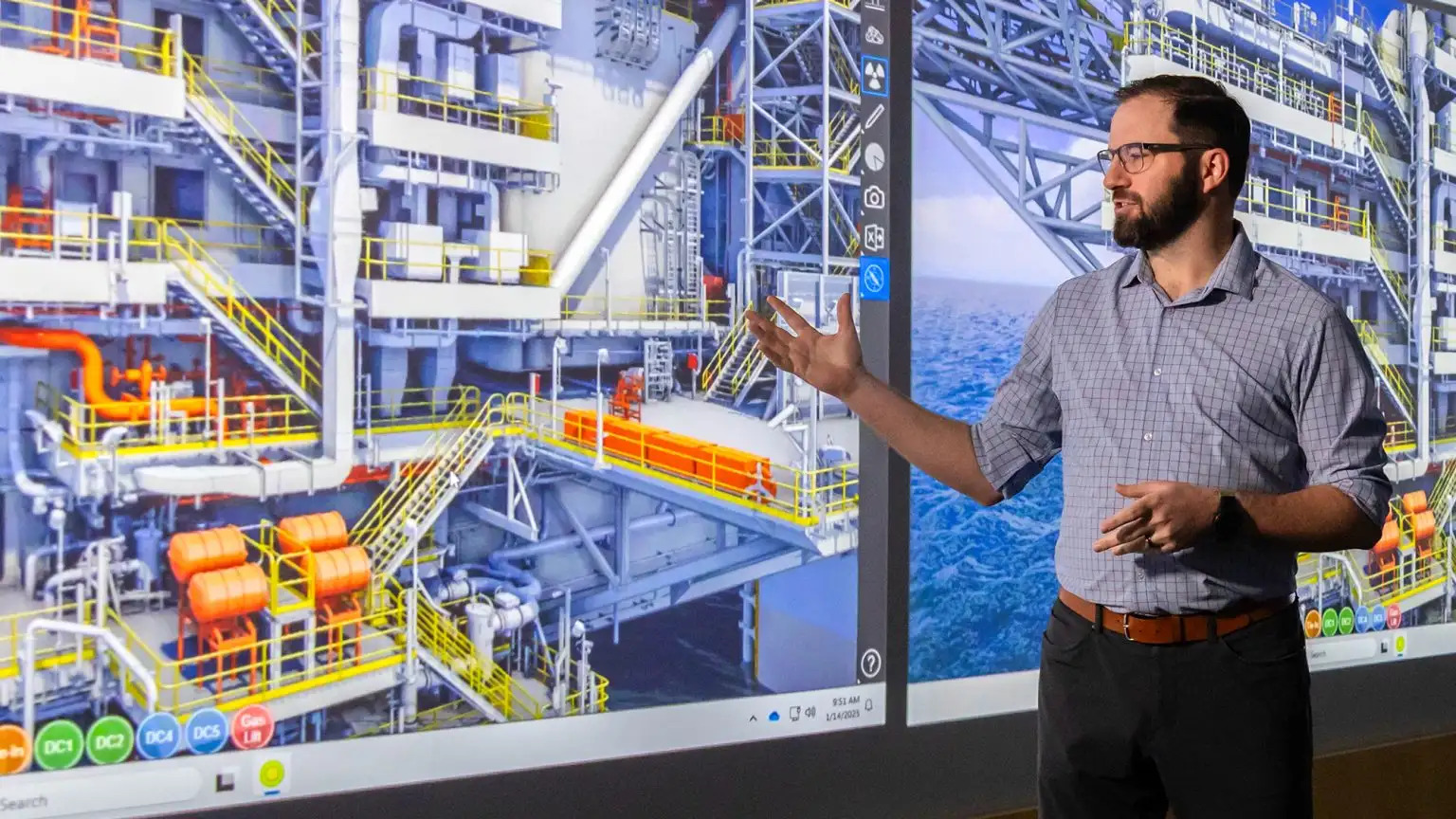 Man presenting in front of large screens showing an offshore oil platform.