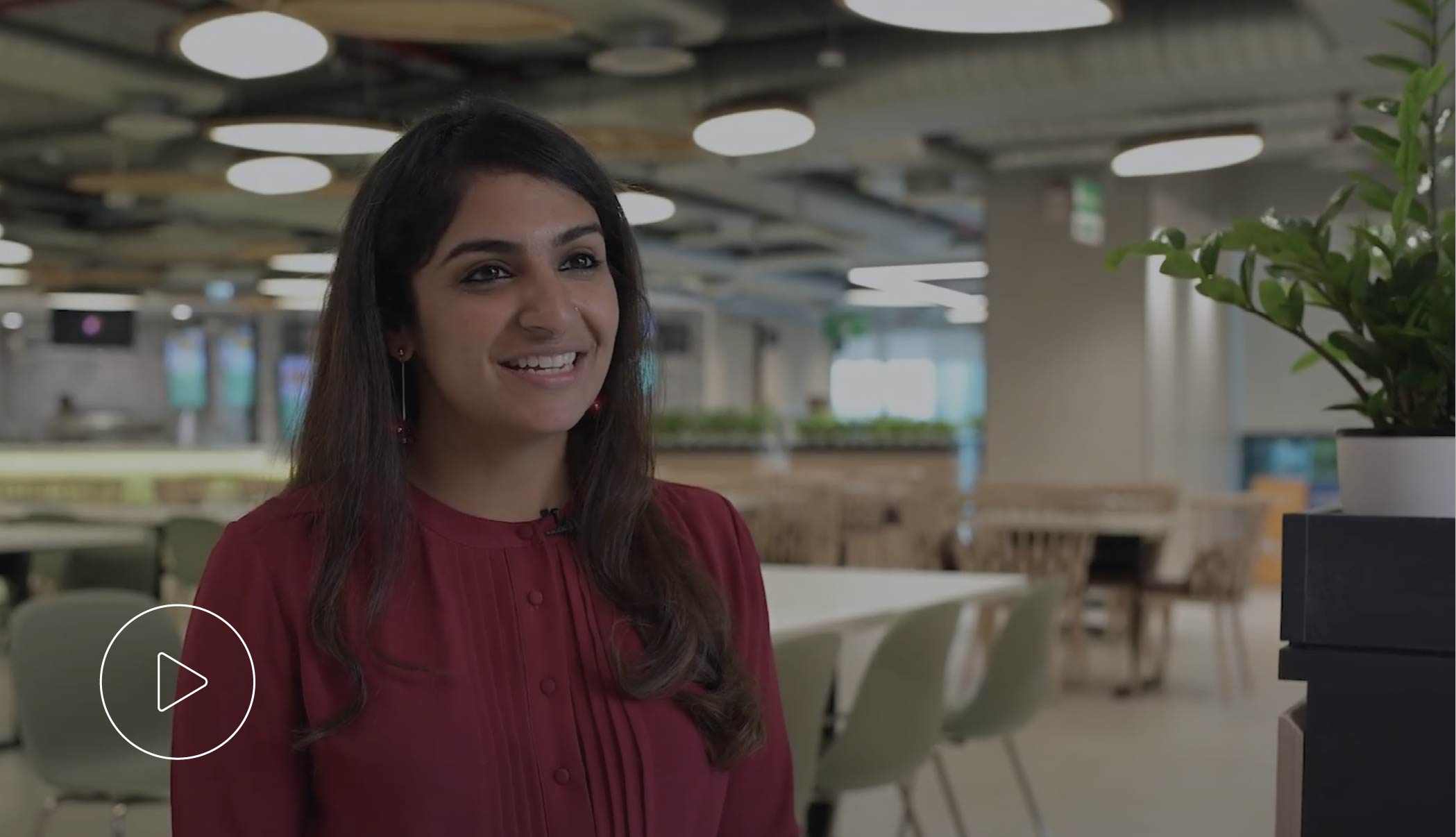 Woman with long dark hair wearing a red blouse, smiling in a modern office setting.