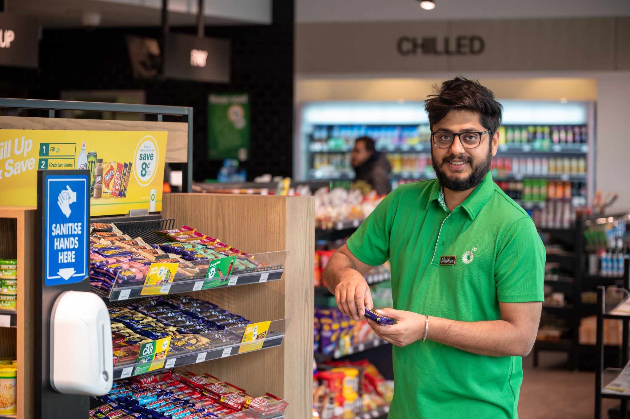 Store employee in green uniform stocking shelves with snacks.