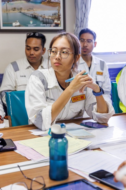 Industrial worker in uniform sitting at a table during a meeting, with documents and a water bottle in front.