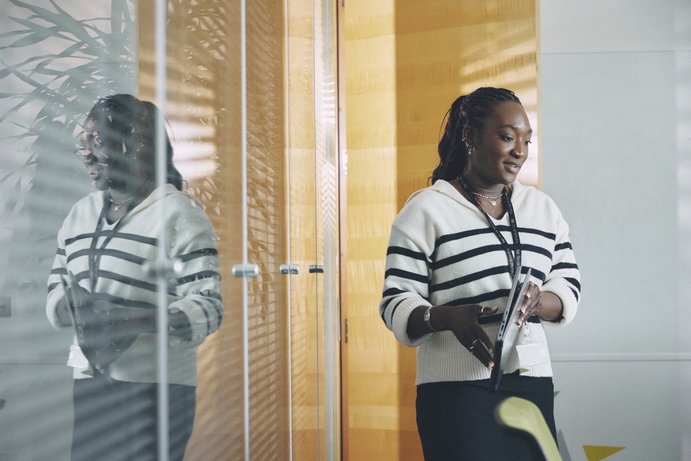 Smiling professional walking through an office hallway holding documents.
