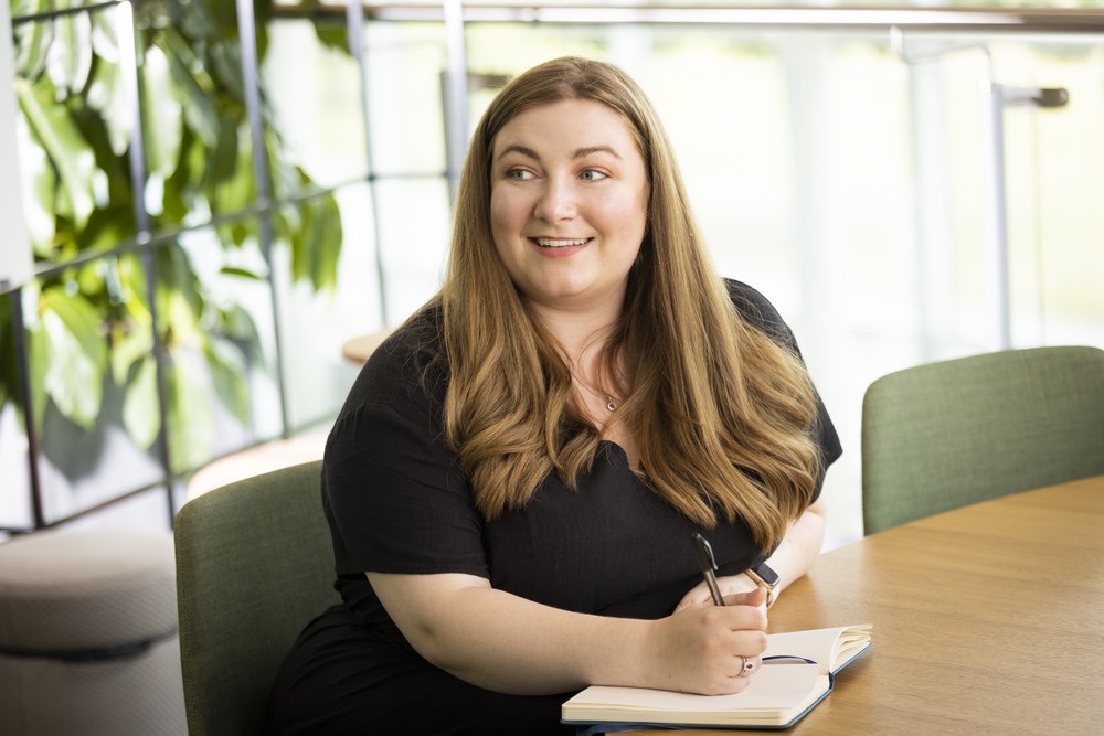 Smiling professional taking notes at a table in a bright office space.