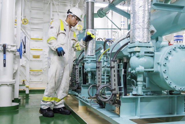 Industrial worker in protective gear inspecting machinery inside a facility.