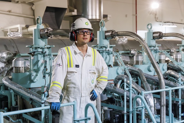 Industrial worker in protective gear inspecting machinery inside a facility.