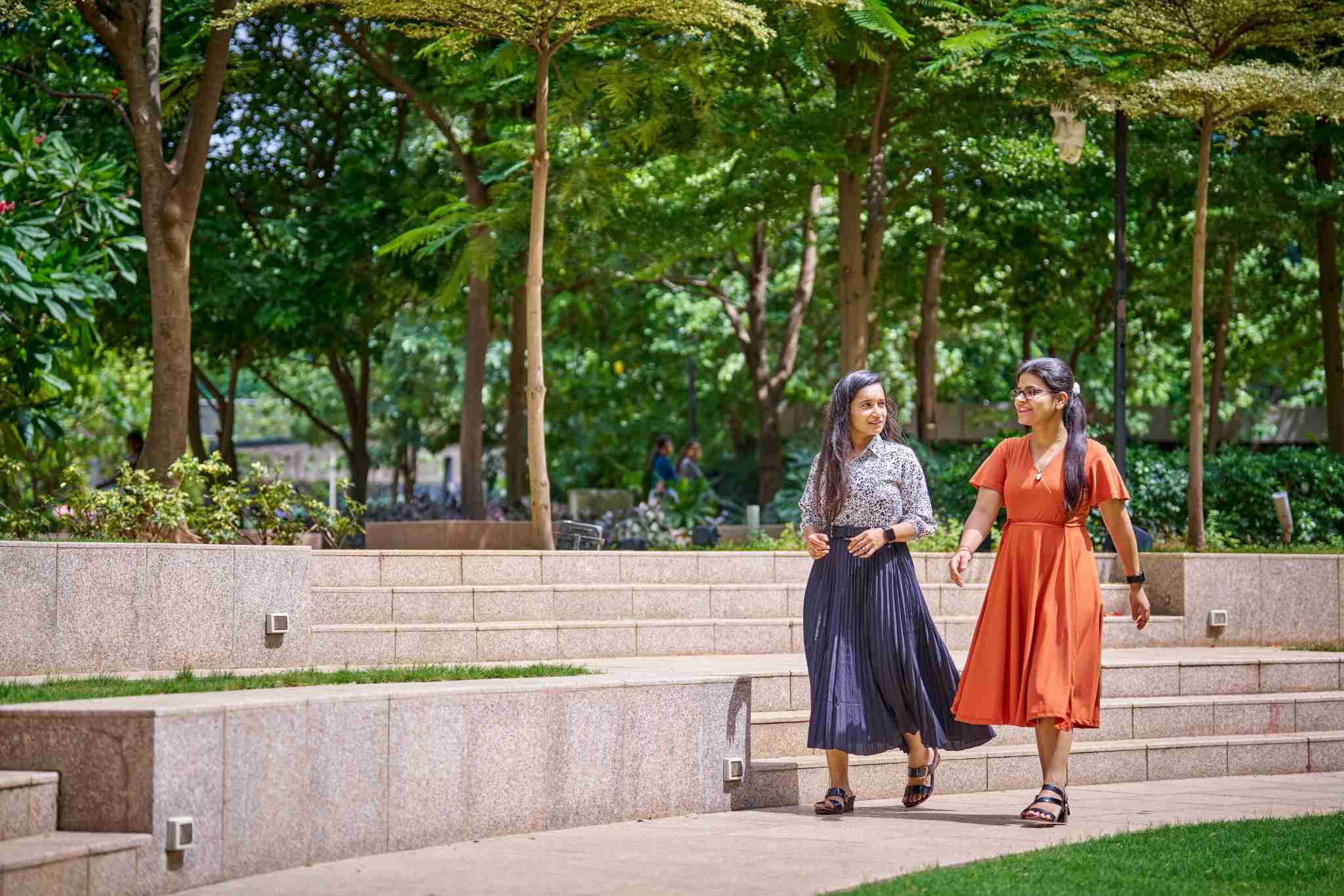 Two women walking outdoors on stone steps in skirts and sandals.