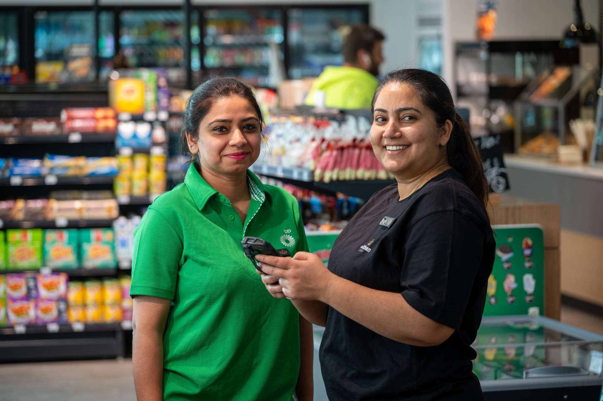 Two smiling store employees standing in front of shelves inside a shop.