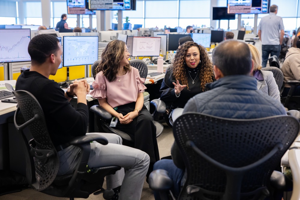 Team members having a discussion in an office with multiple computer monitors.