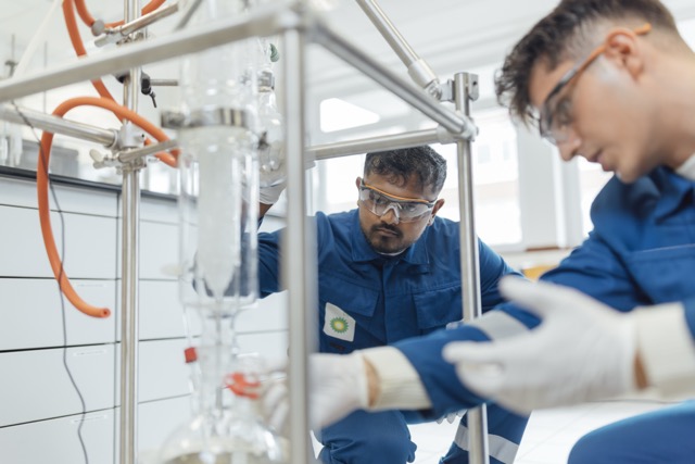 Two bp lab technicians in protective gear working with scientific equipment in a laboratory.