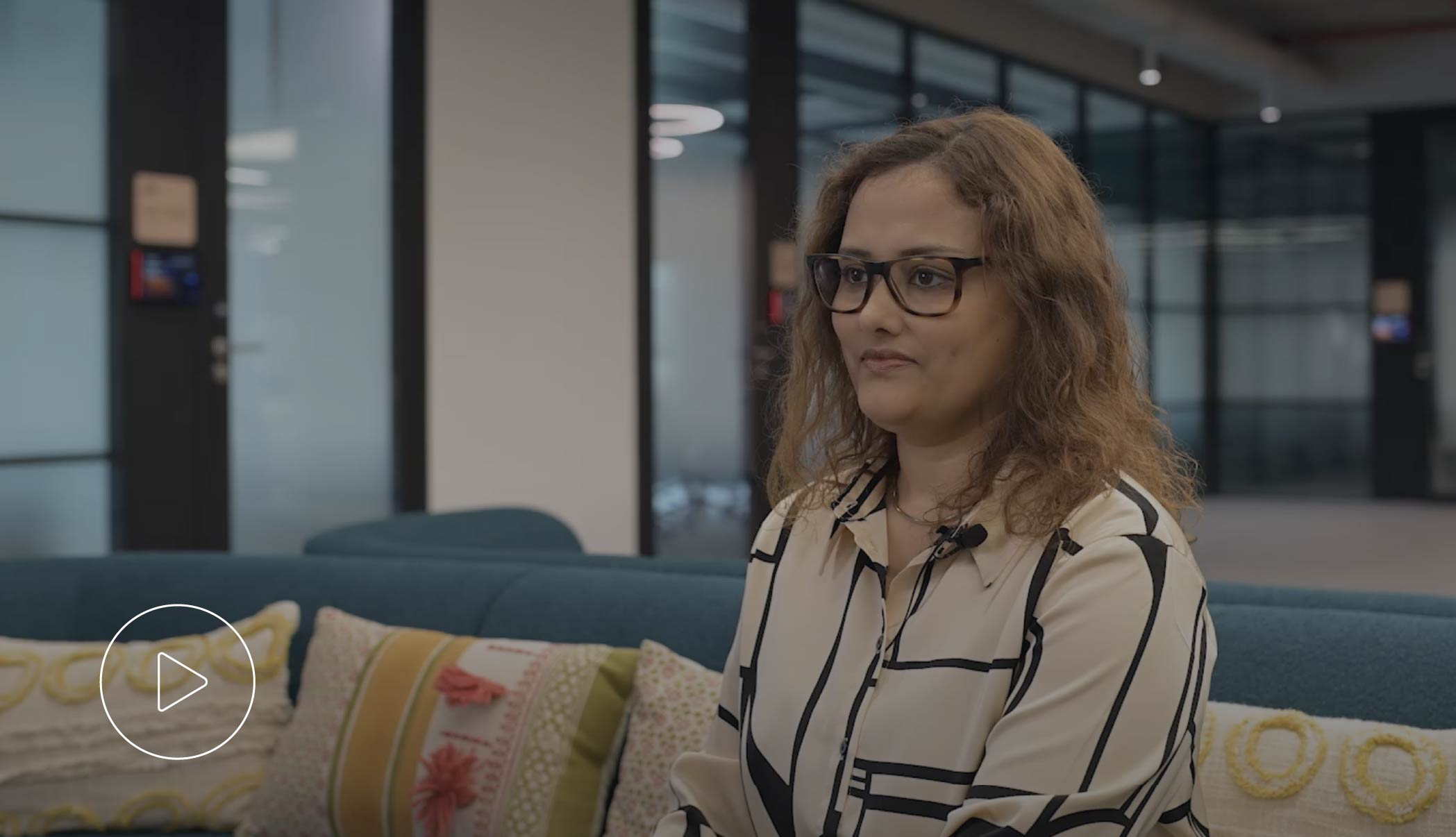 Woman wearing glasses sitting on a blue sofa in a modern office setting