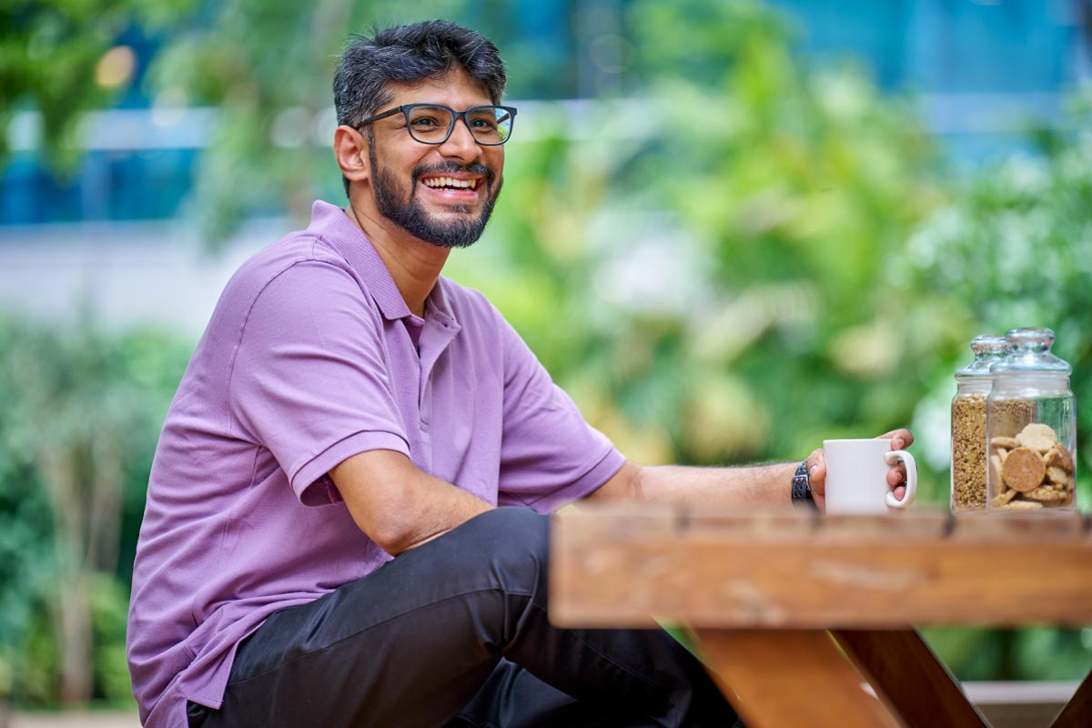 Smiling man wearing glasses and a purple shirt sitting outdoors.