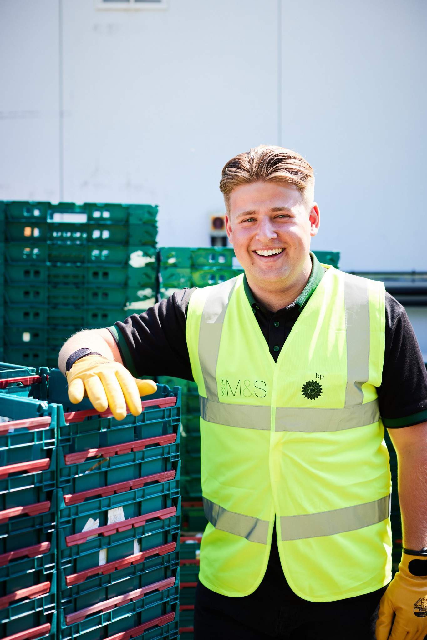 Smiling worker in high-visibility vest standing by stacked crates.