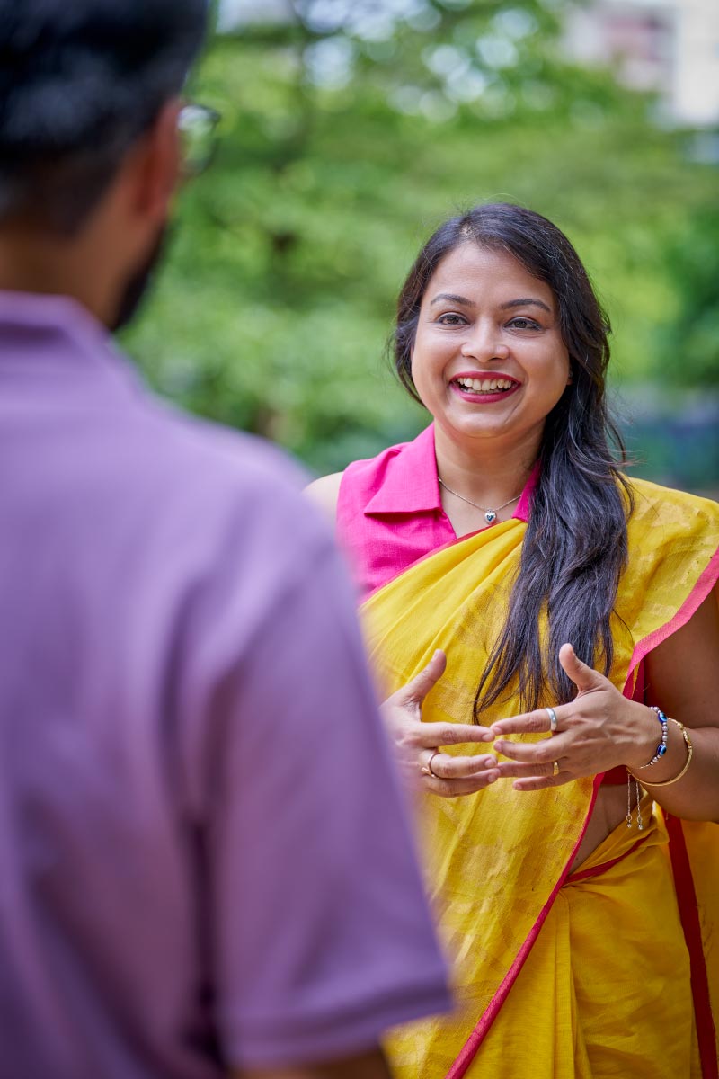 Smiling woman in yellow sari talking with colleague outdoors.