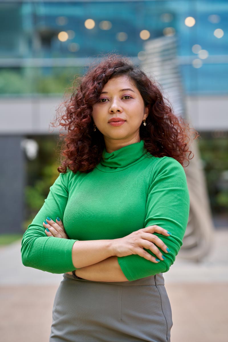 Professional portrait of woman with curly hair standing outdoors.