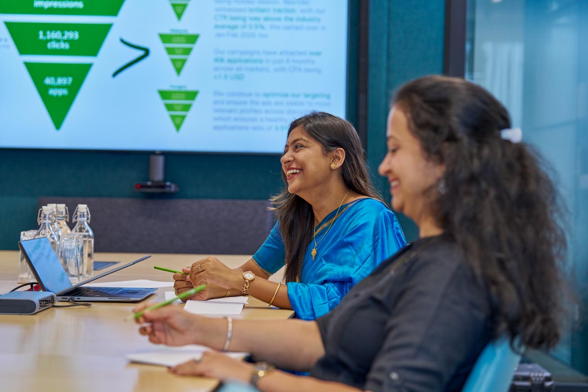 Two women smiling during a meeting with notebooks and pens on table.