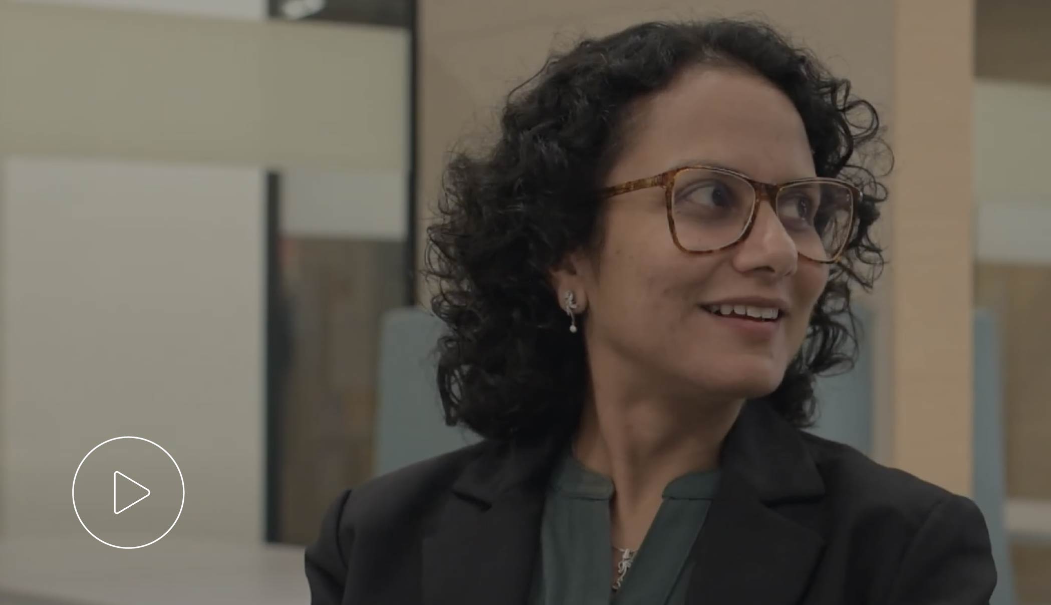 Seema, a senior manager of corporate partnerships, smiling. She is seated at a table in an office lounge area.