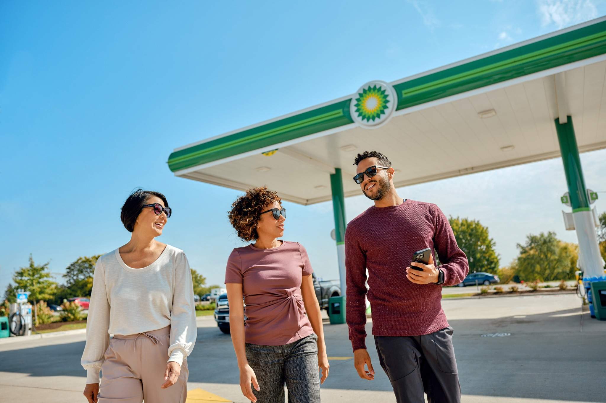 Three people walking and smiling near a bp gas station.