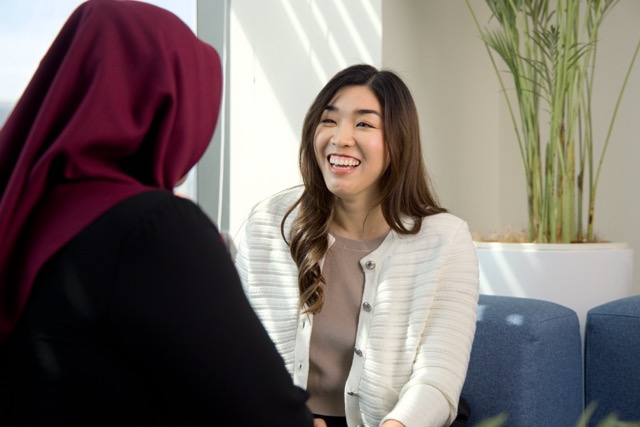 Smiling female employee in a white jacket talking with a colleague in an office setting.