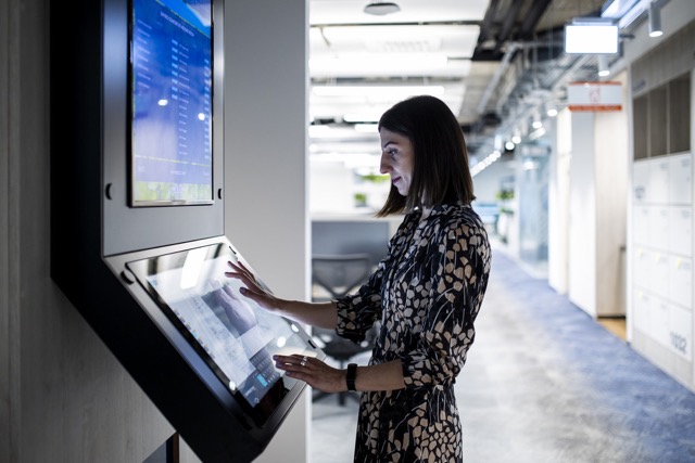 Female employee using a touchscreen display in a modern office environment.