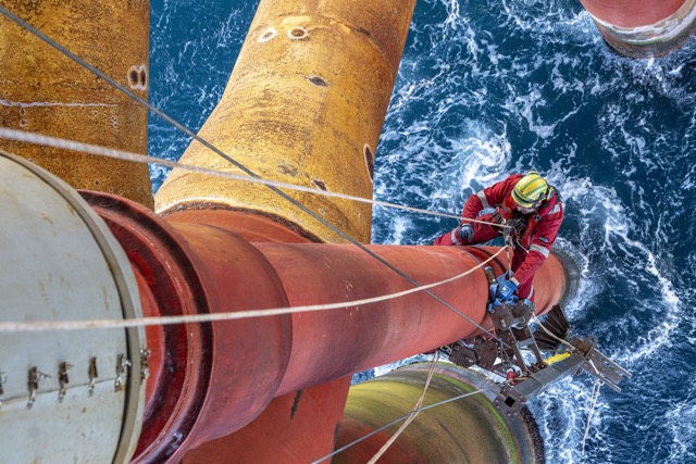 bp offshore worker in protective gear maintaining oil rig structure above sea, highlighting safety and energy.