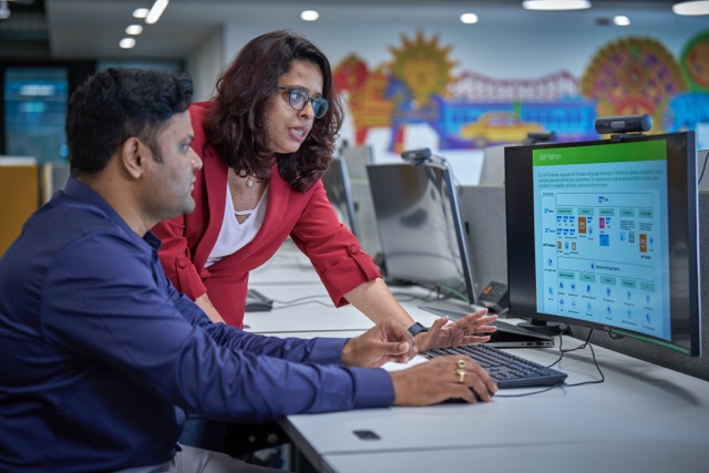 Two employees collaborating at a computer, reviewing an SAP platform screen in a colorful office.