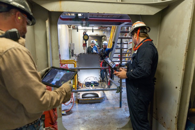 Employees in safety gear operating equipment and monitoring a worksite inside an industrial facility.