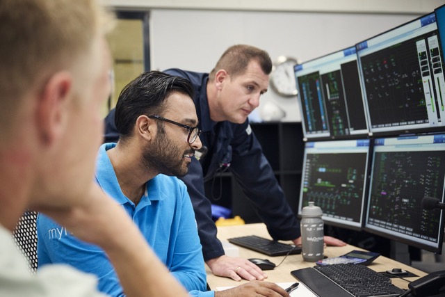 Employees monitoring multiple control room screens while collaborating on operations.