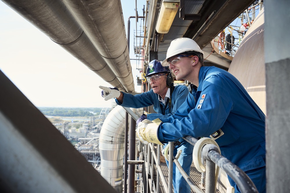 Two industrial engineers in protective gear inspecting and discussing operations at an oil and gas facility.