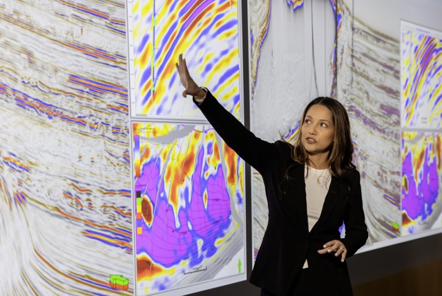 Female geoscientist presenting seismic data and geological models on large digital screens in an energy research center.