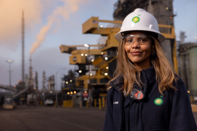 Female bp engineer wearing safety helmet and protective glasses at oil refinery plant during sunset, representing energy innovation and workplace safety.