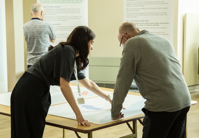 Two colleagues reviewing project plans together at a table in a bright office setting.