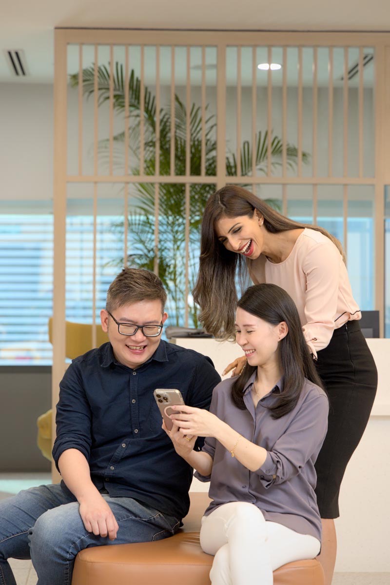 Diverse team of three colleagues smiling and collaborating together in a modern office environment.