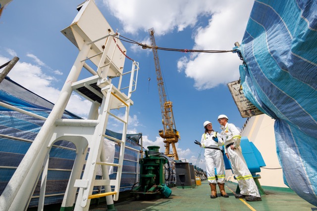 Two engineers in safety gear discussing operations at an industrial site with cranes and heavy equipment.