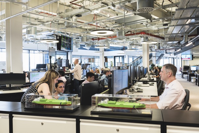 Employees working at desks in modern office with ship models on display.