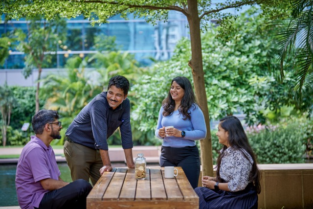 bp employees enjoying coffee break outdoors, smiling and connecting at picnic table, reflecting teamwork and wellbeing.