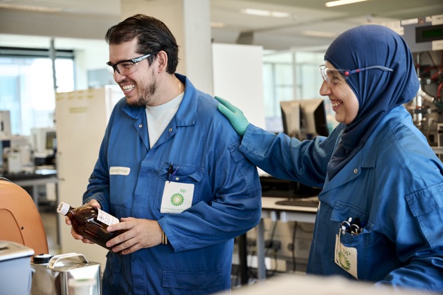 bp laboratory scientists in blue protective coats smiling while working with chemical samples, showcasing teamwork and innovation in energy research.
