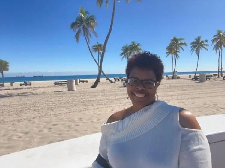 Woman smiling at beach with palm trees and blue sky background.