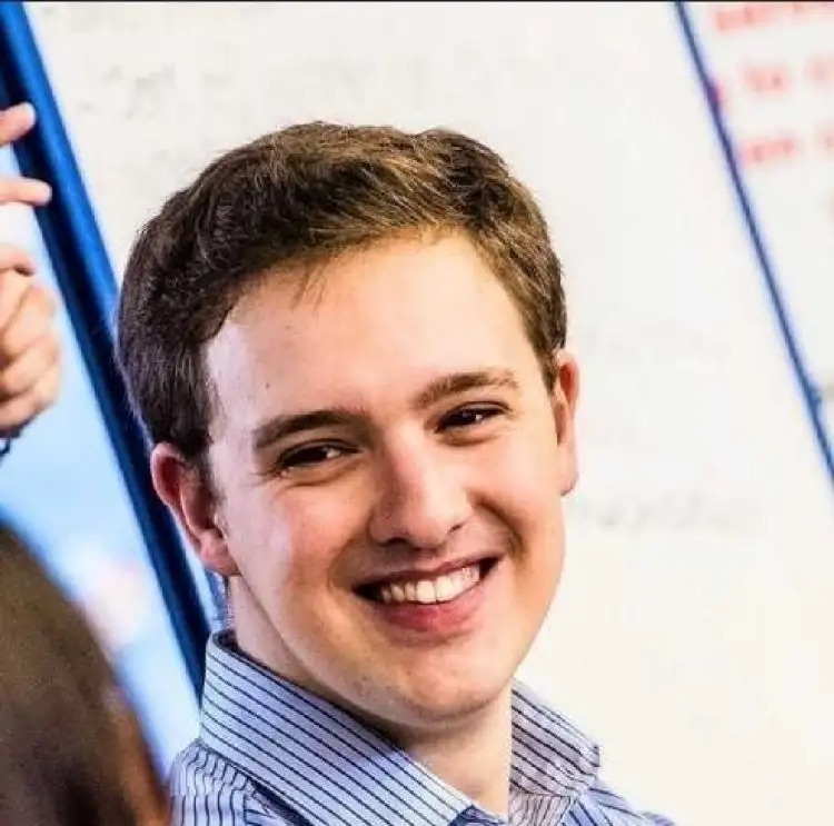 Smiling man in office meeting, whiteboard in background.