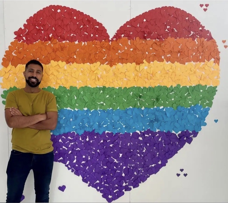 Man standing in front of rainbow heart wall art.