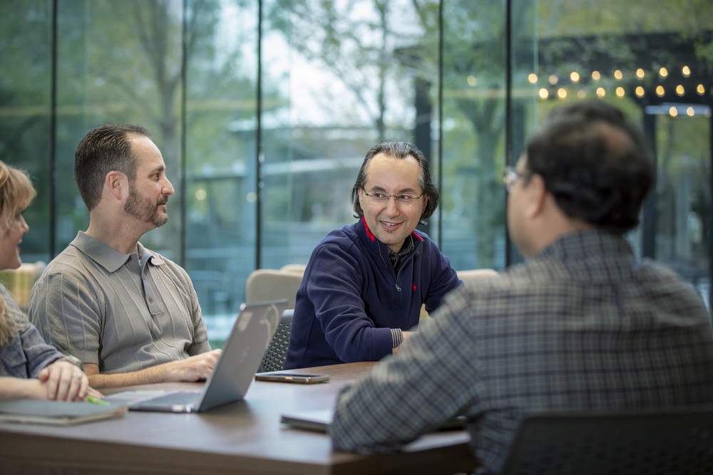Diverse professionals engaged in a collaborative business meeting in a modern office with glass windows.