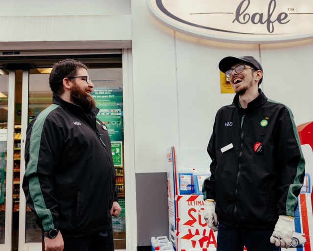 Two bp employees in uniform smiling and talking outside a convenience store.