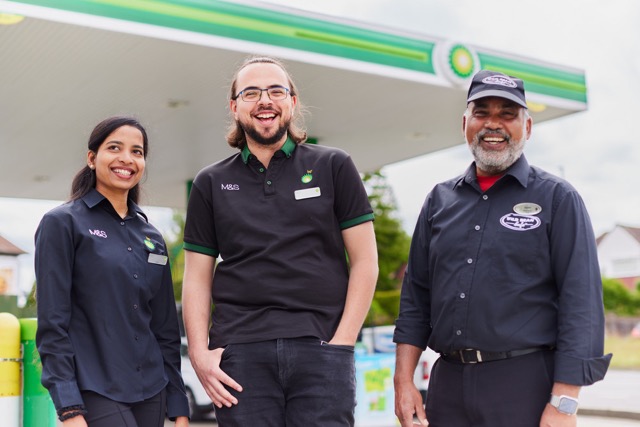 Three bp employees standing outside a gas station, smiling at the camera.