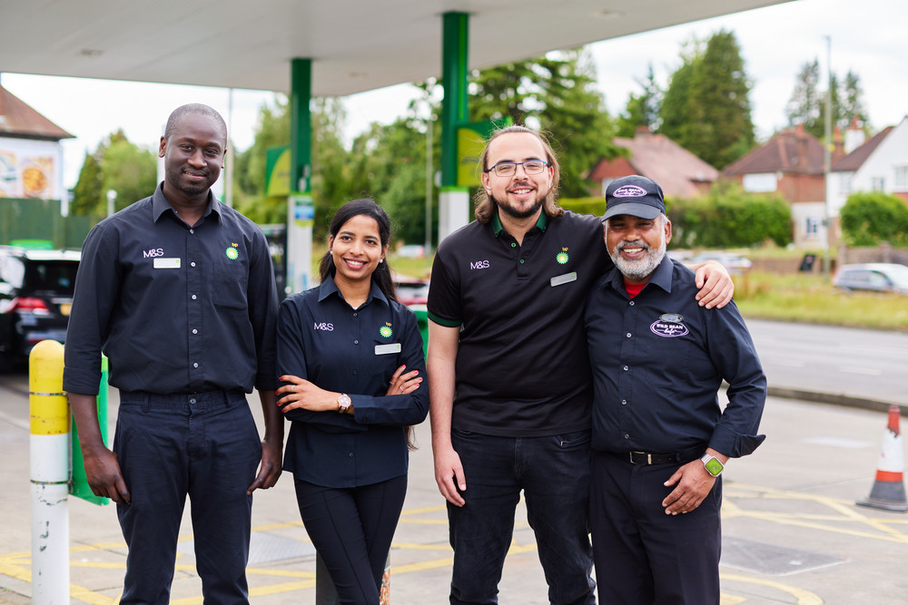 Diverse bp and M&S service station team smiling together at a forecourt.