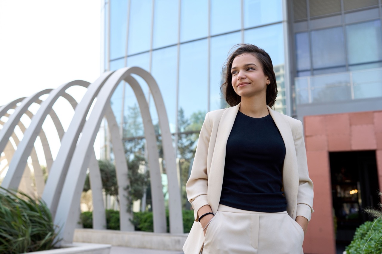 Person standing confidently outdoors near a modern building with arched structures.