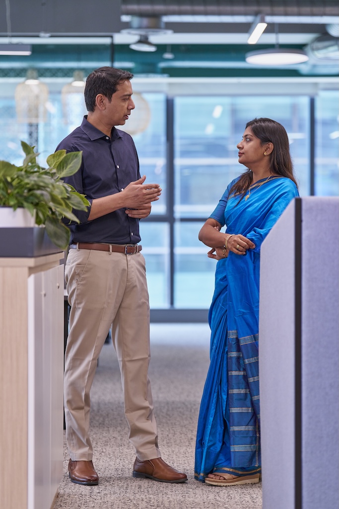 Man and woman having a conversation in a modern office setting with plants in the foreground.
