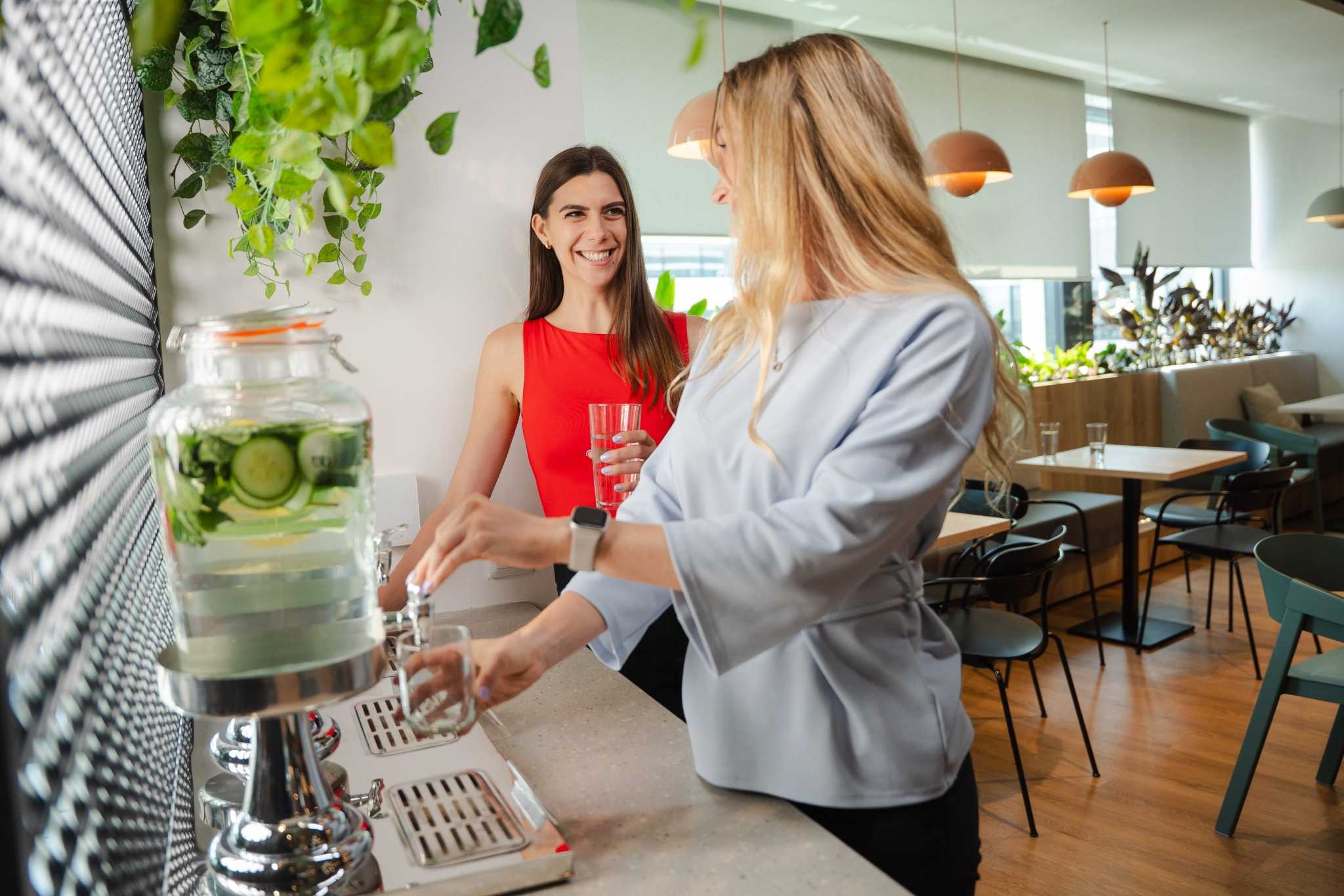 Two colleagues chatting while filling water in a modern office kitchen.