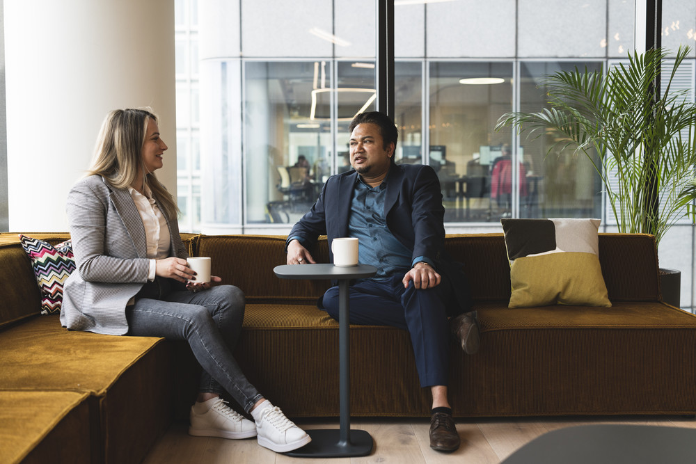 Two colleagues having a coffee and conversation in a modern office lounge.